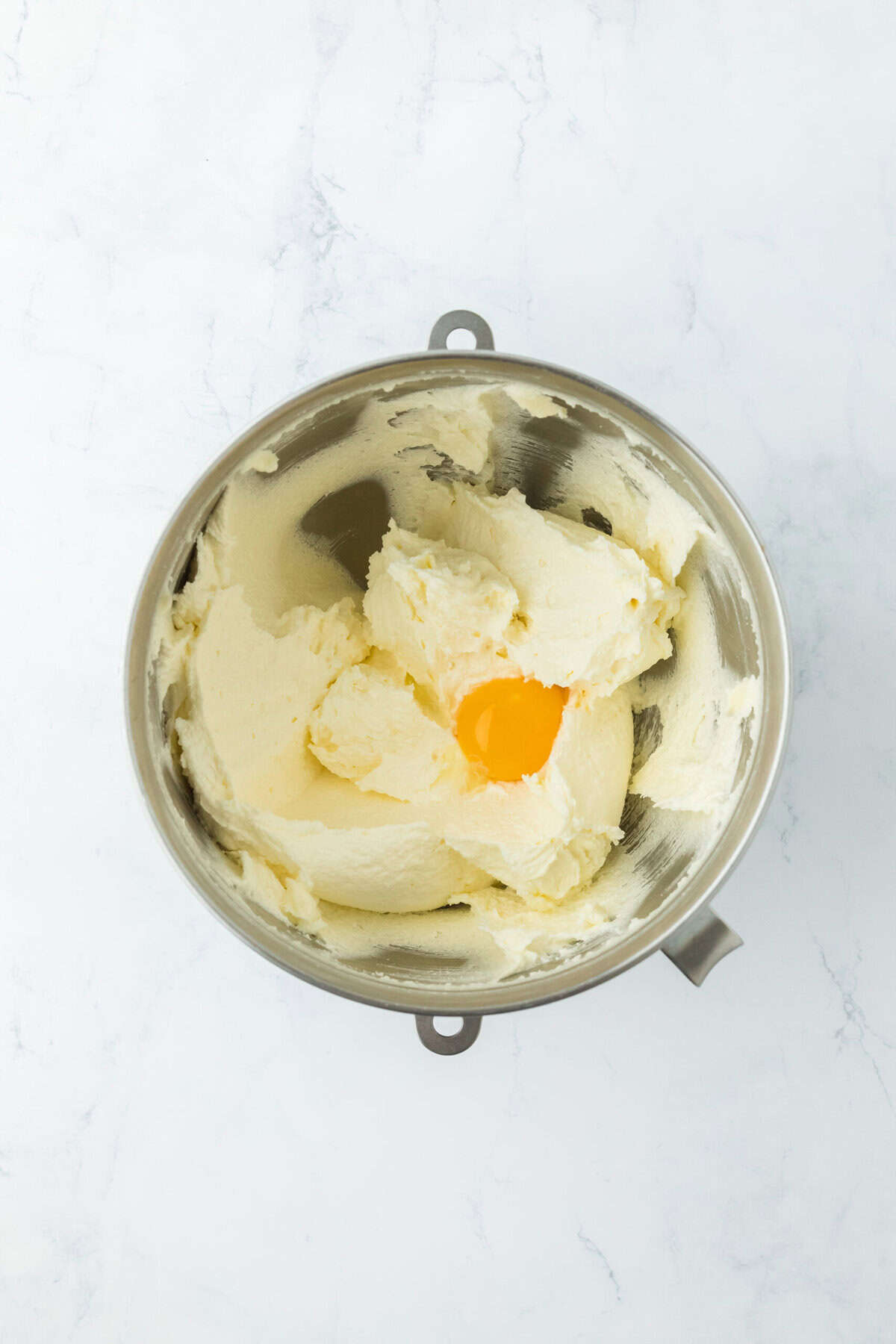 Eggs being added to creamed butter and sugar in a stand mixer bowl on white countertop