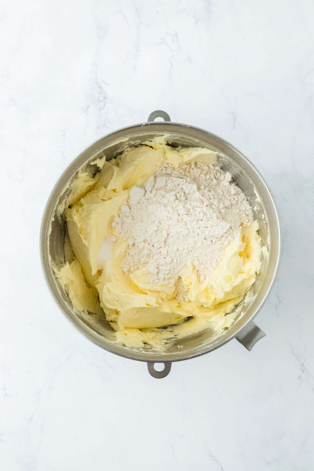 Flour being added to stand mixer bowl to make pound cake batter on white countertop