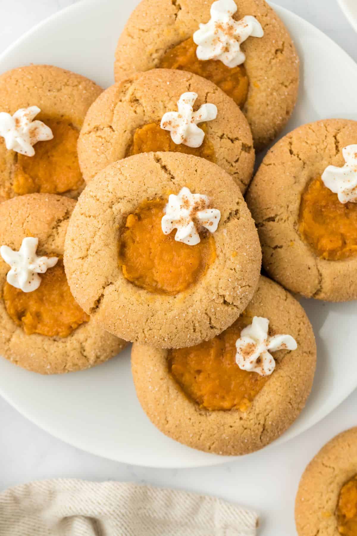 Closeup of sweet potato pie cookies on a plate, topped with dollops of whipped cream and a sprinkle of cinnamon