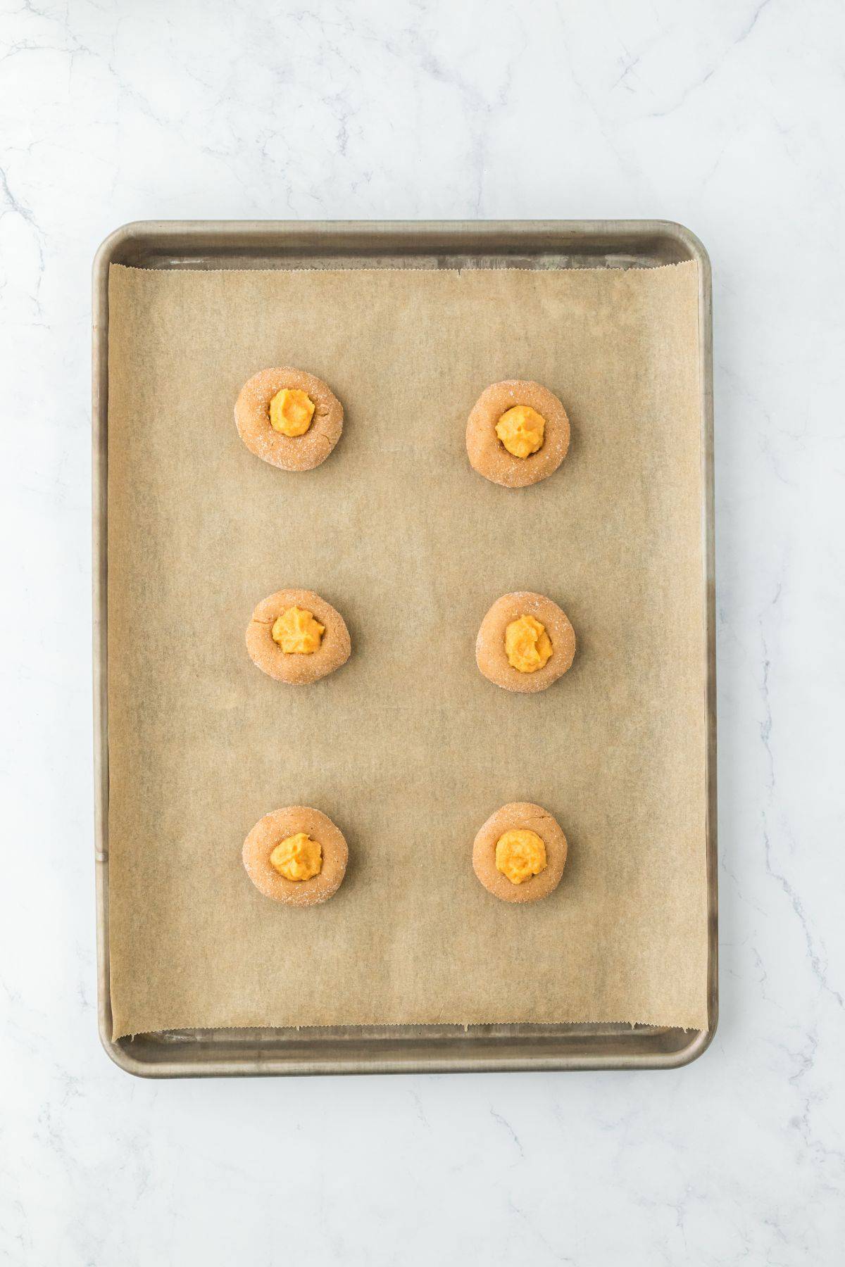 Prepared cookie dough with sweet potato filling piped into the centers, arranged on a baking sheet