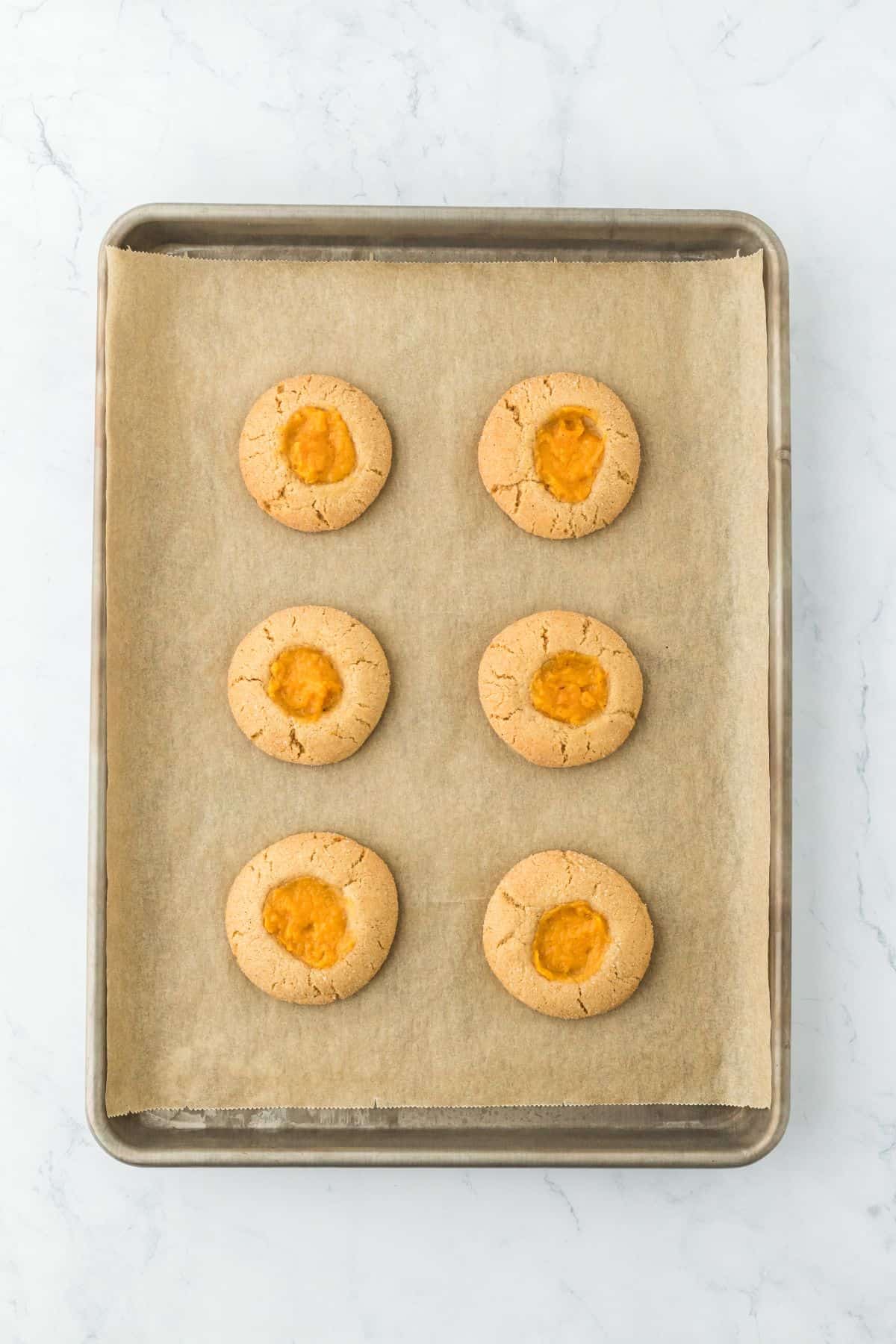 Six baked sweet potato pie cookies on a parchment-lined baking sheet