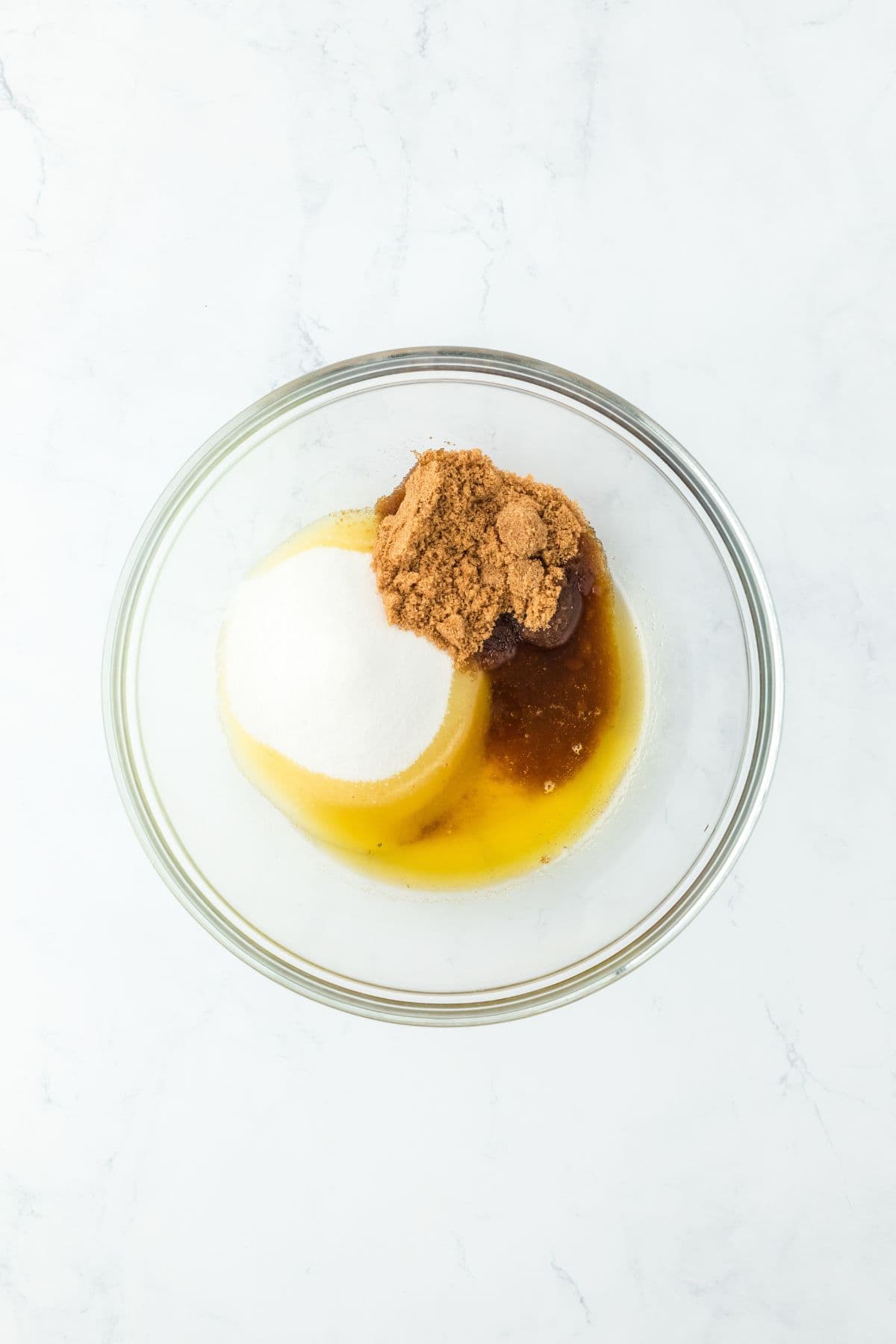 Mixing bowl with brown sugar, white sugar, and melted butter for cookie dough preparation