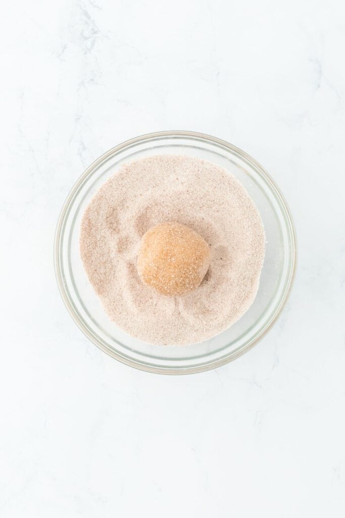 Dough ball being rolled in cinnamon sugar for a flavorful coating