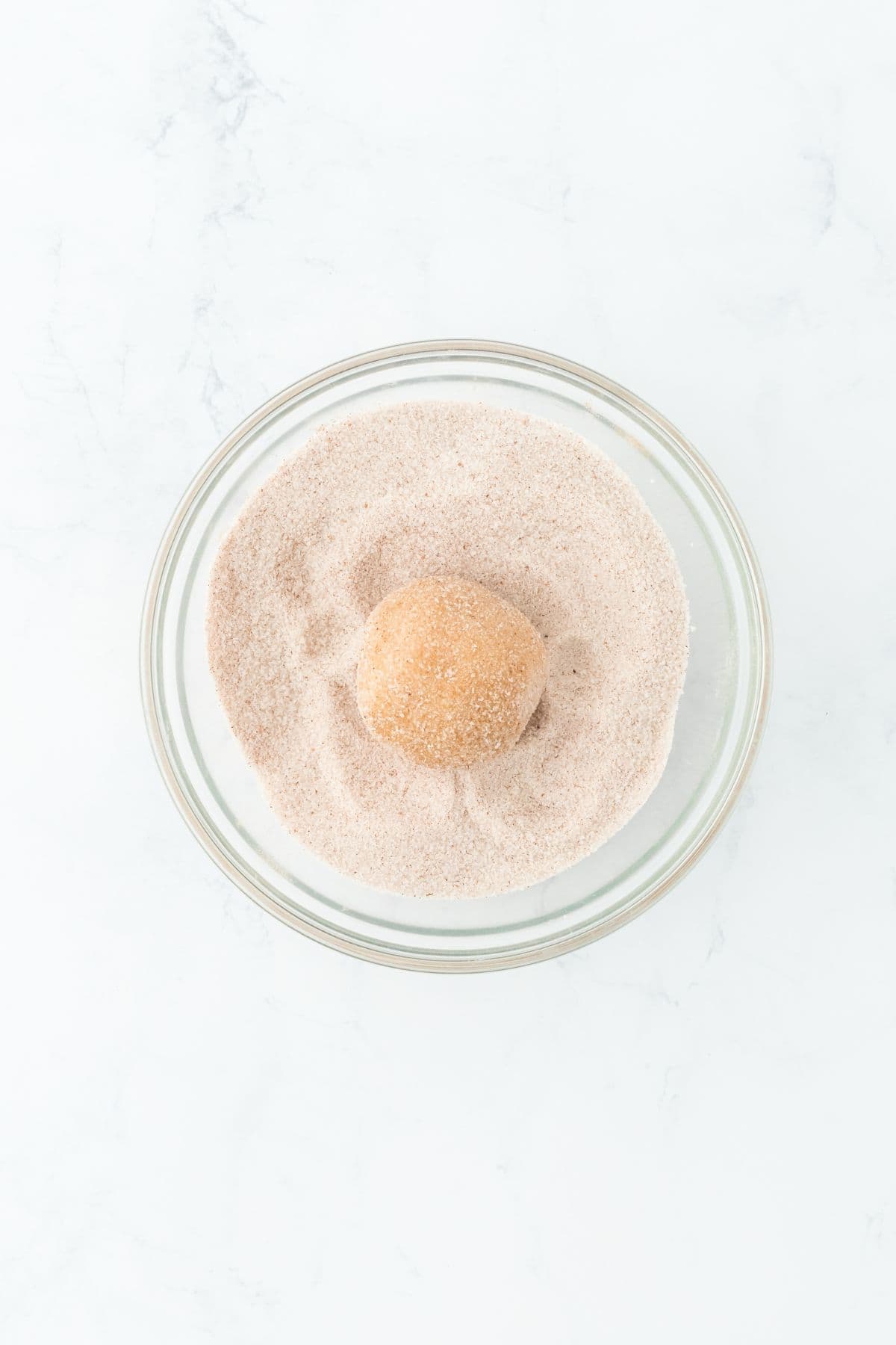 Dough ball being rolled in cinnamon sugar for a flavorful coating