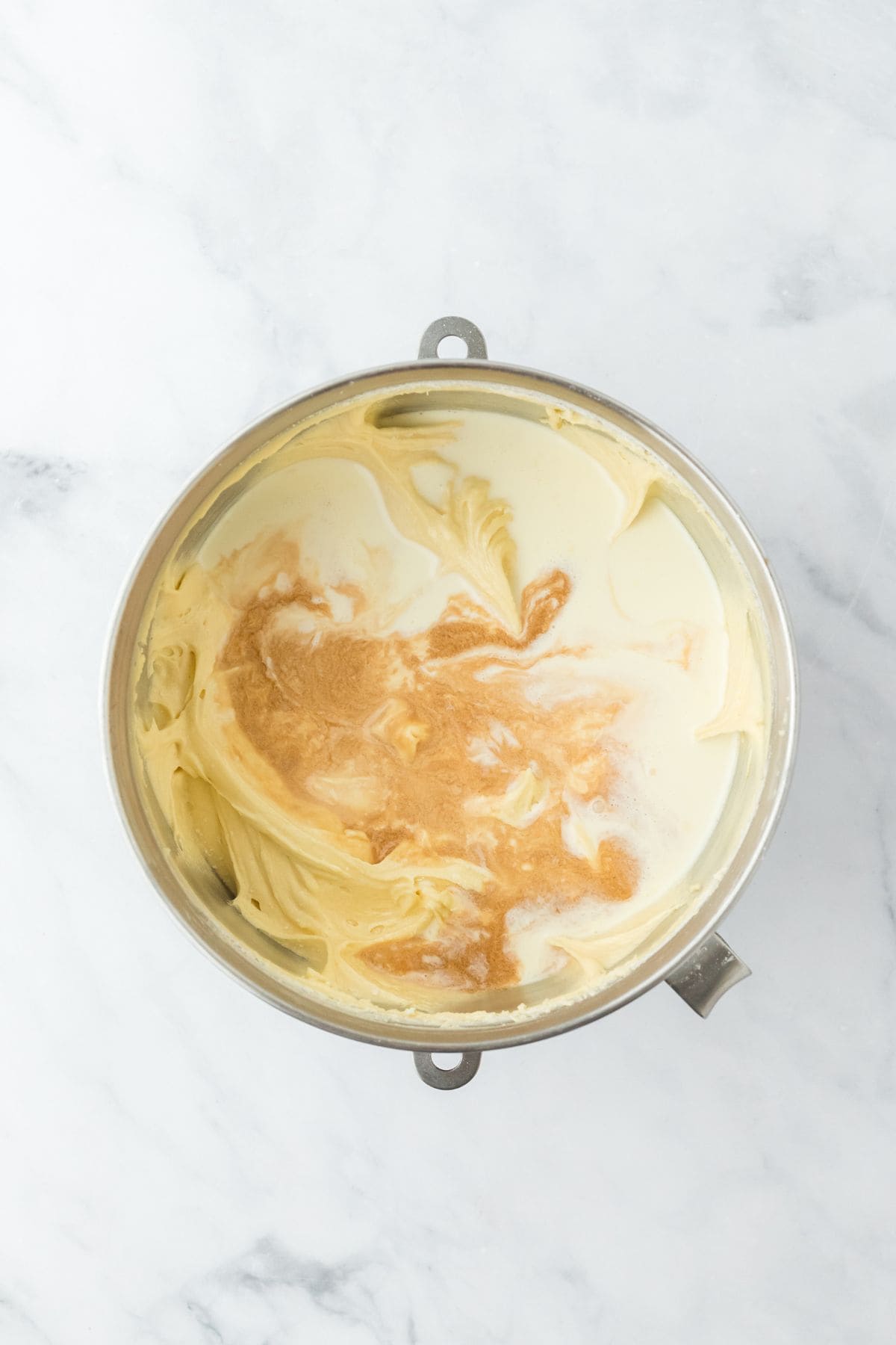 A mixing bowl with wet ingredients, including vanilla and cream, added to the batter