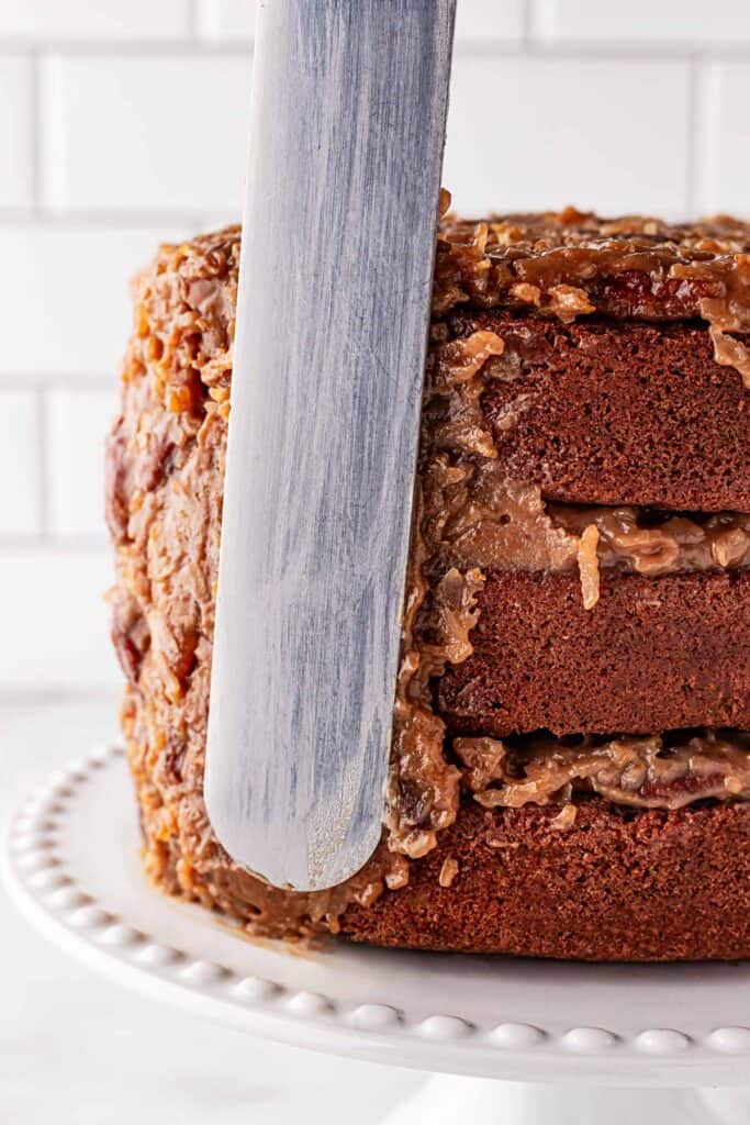 Icing the sides of German chocolate cake on white cake stand