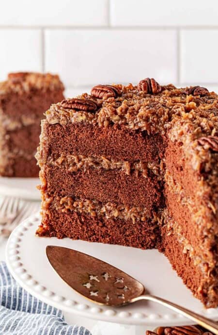 Sliced open German chocolate cake on white cake stand with gold cake cutter