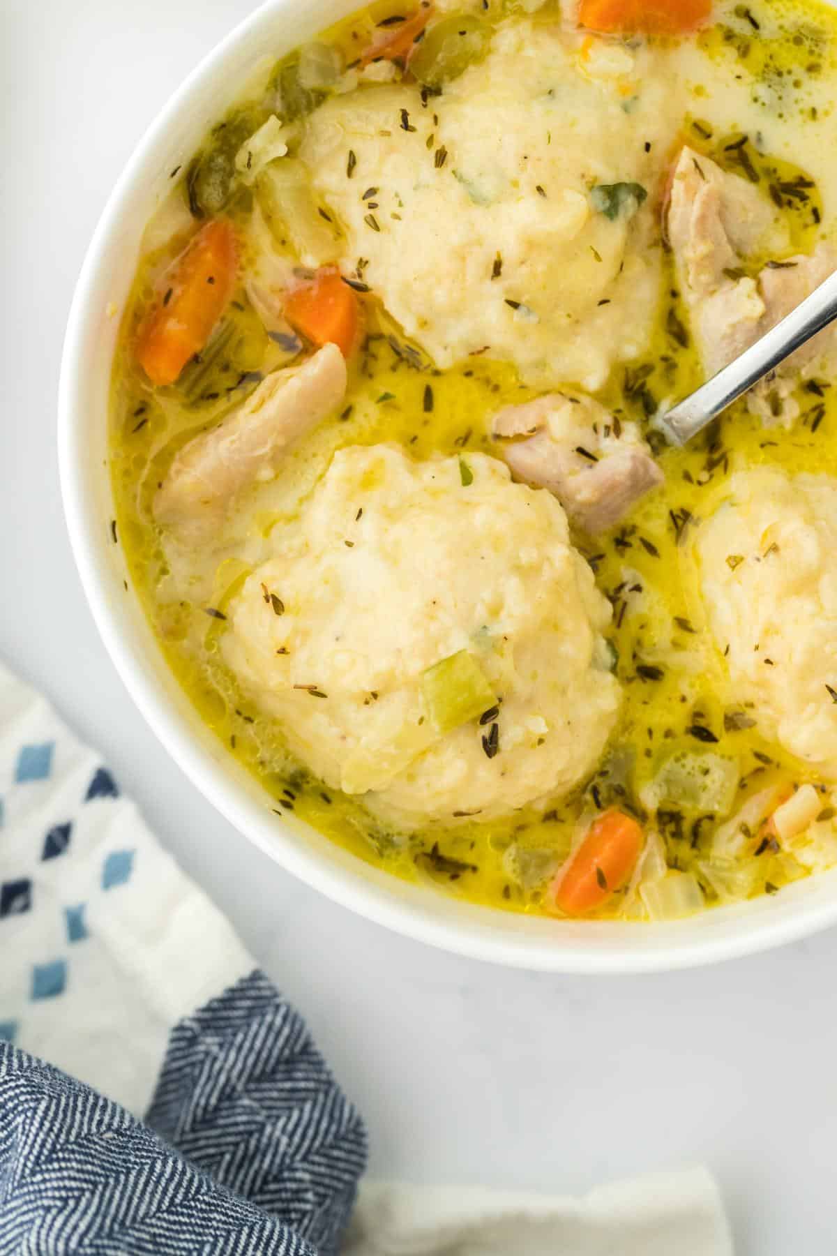 Overhead shot of a bowl filled with chicken and dumpling soup, showcasing tender chicken chunks, fluffy dumplings, and a creamy broth with vegetables