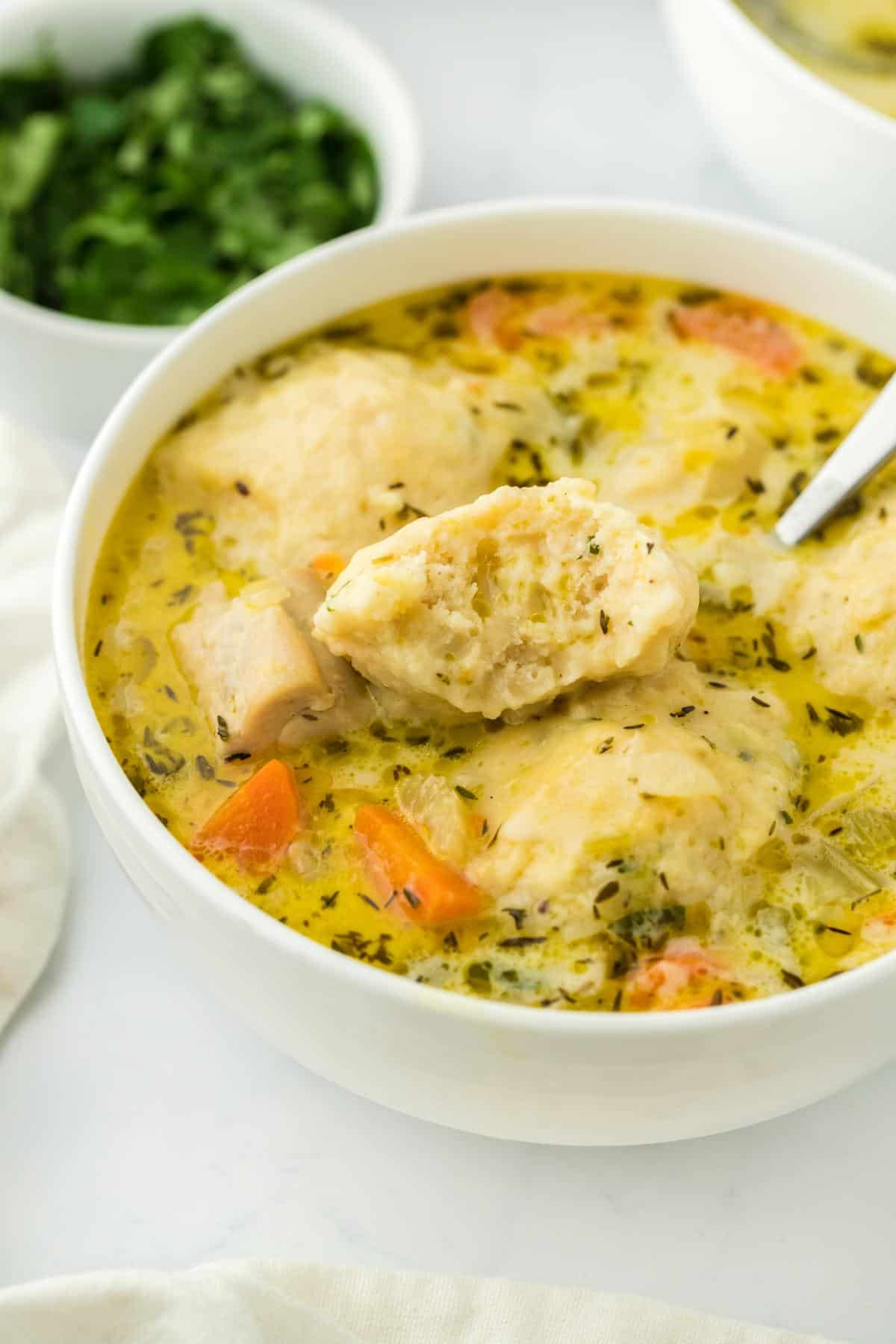 A closeup of a dumpling being split open, revealing its fluffy, tender interior, with the soup in the background