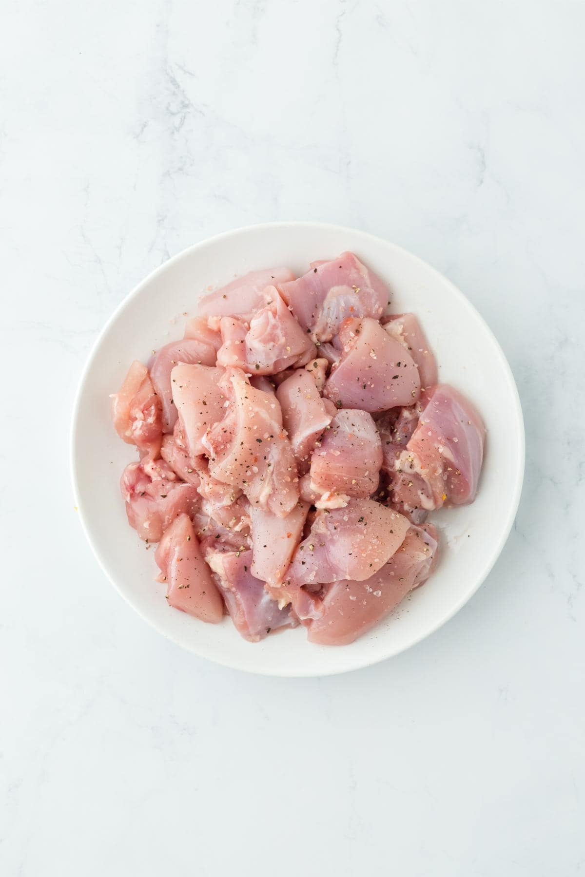 A bowl of raw, seasoned chicken pieces on a white plate