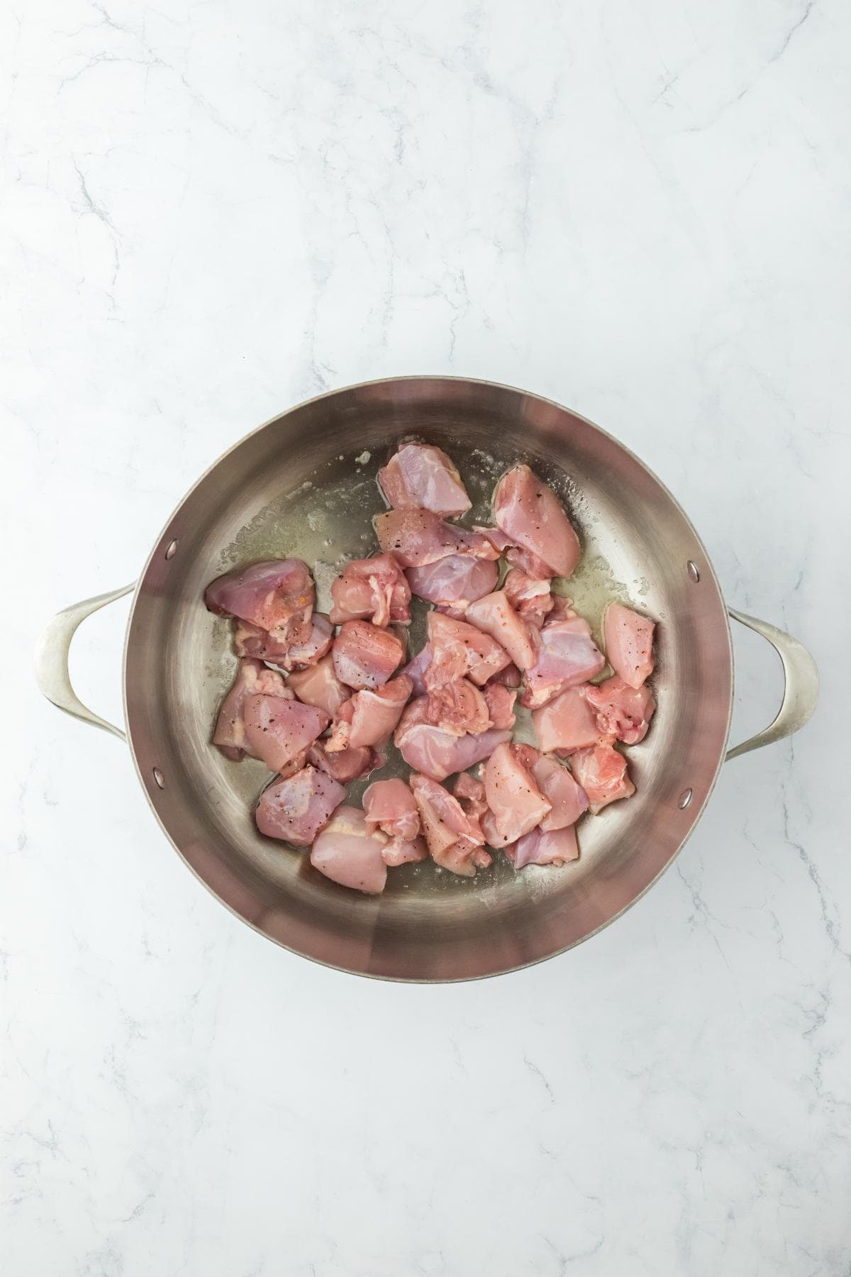 Raw chicken pieces in a stainless steel pot, ready to cook