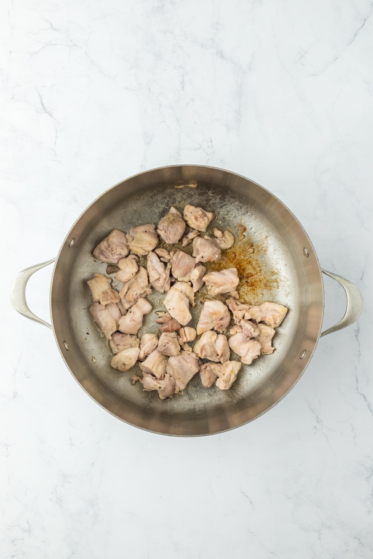 Partially cooked chicken pieces in a pot with some browning visible