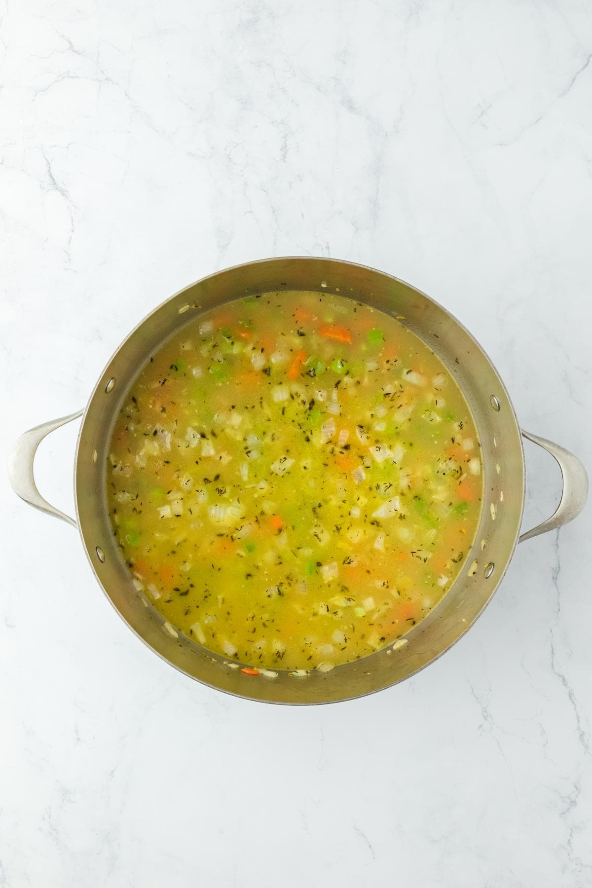 A pot with broth and vegetables starting to simmer