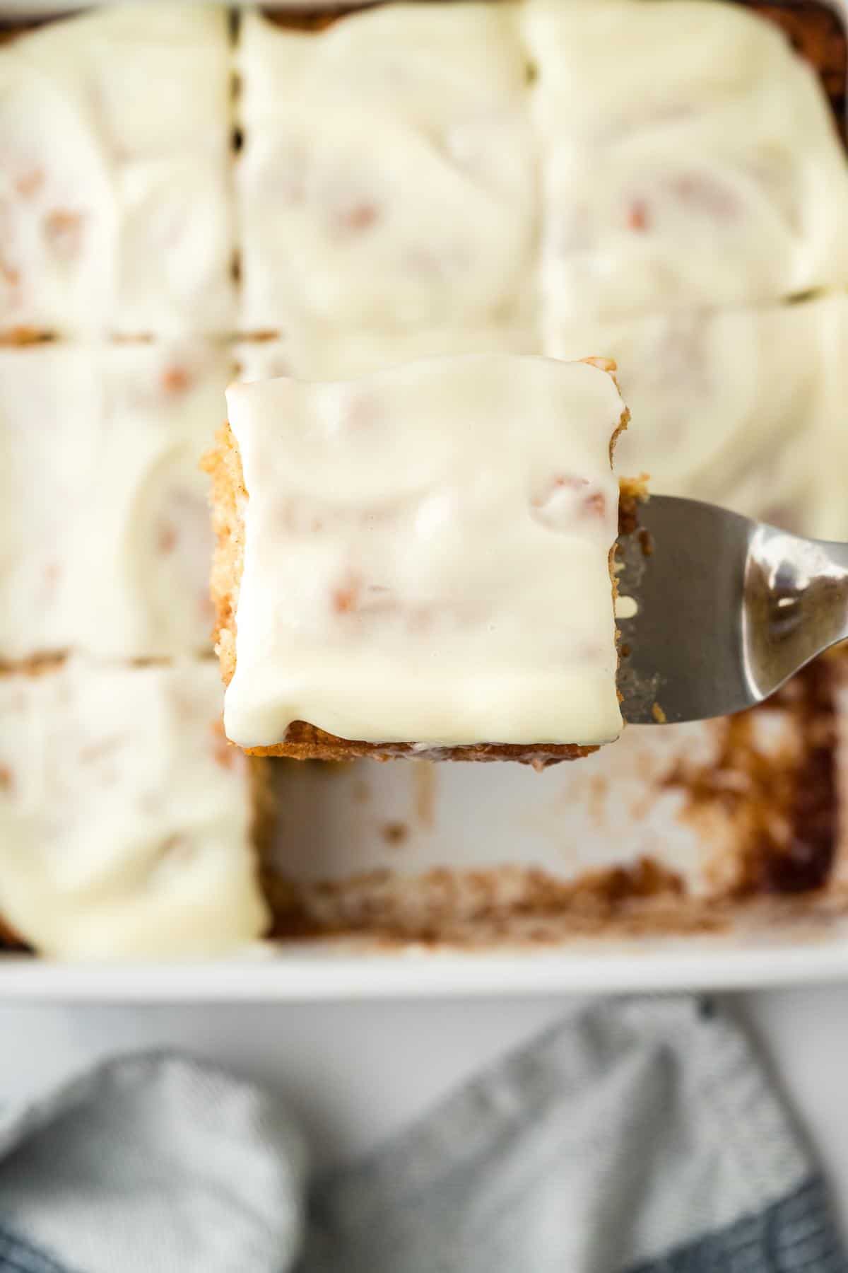 Overhead shot of a frosted cinnamon roll butter swim biscuit being lifted from the baking dish with a spatula