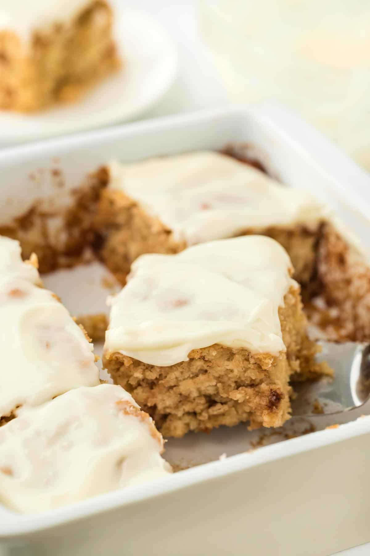 A single serving of cinnamon roll butter swim biscuits being lifted with a spatula from the baking dish, showing the smooth, creamy topping