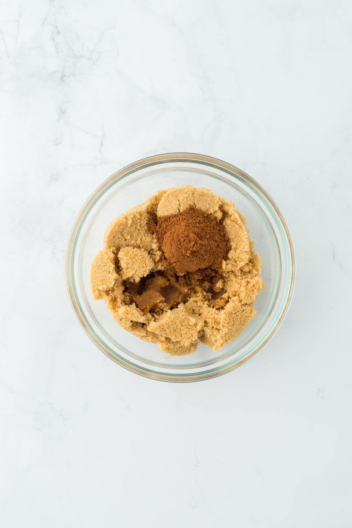 A glass bowl containing brown sugar and cinnamon before being mixed