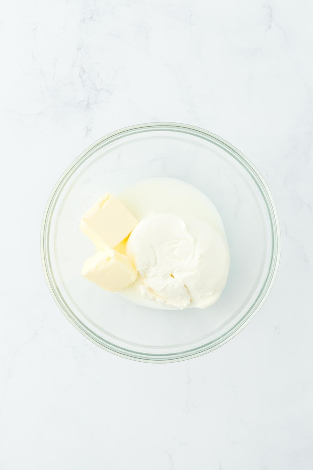 A glass bowl with cream cheese, butter, and milk