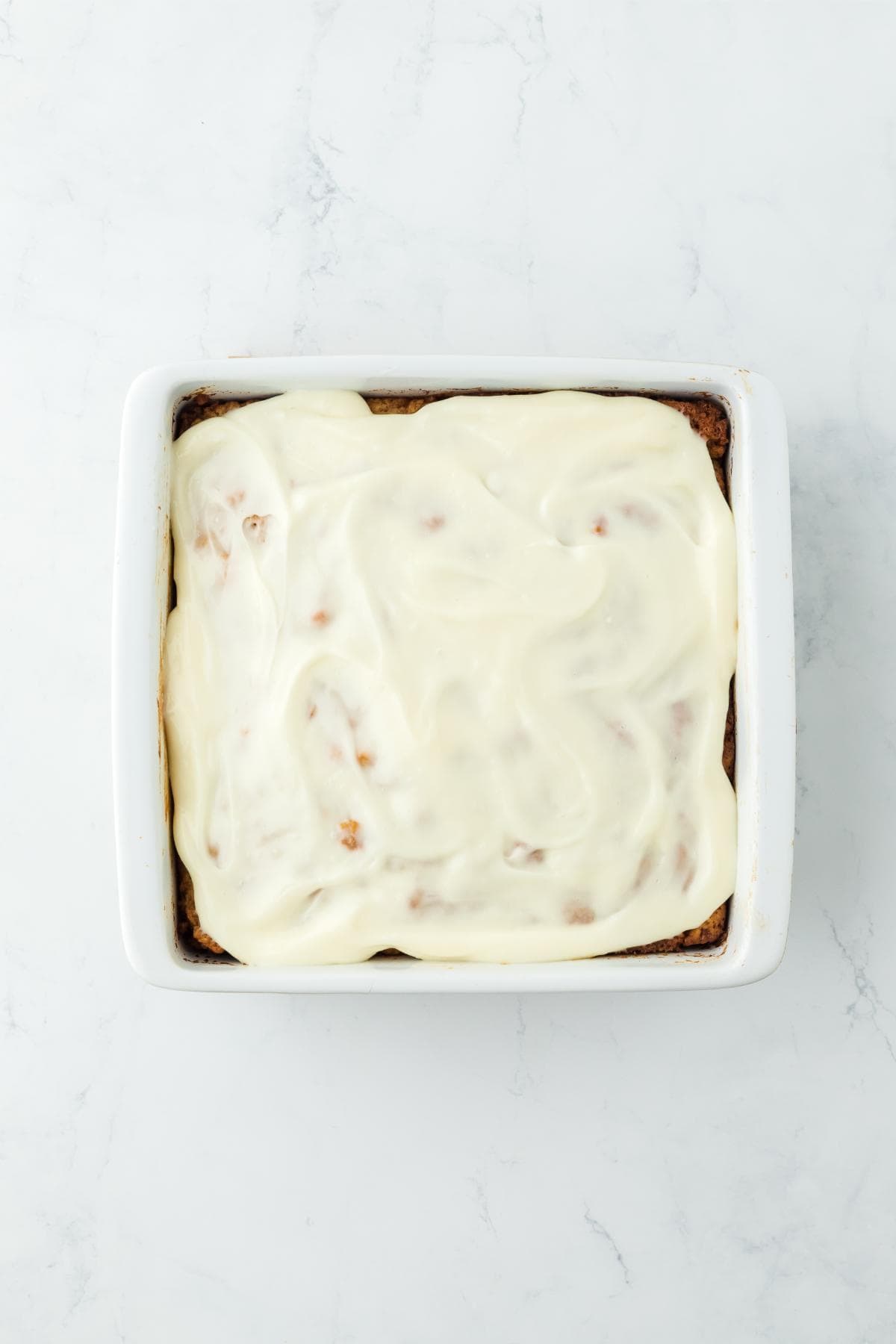 The baking dish with the baked cinnamon roll butter swim biscuits fully covered in smooth, creamy frosting