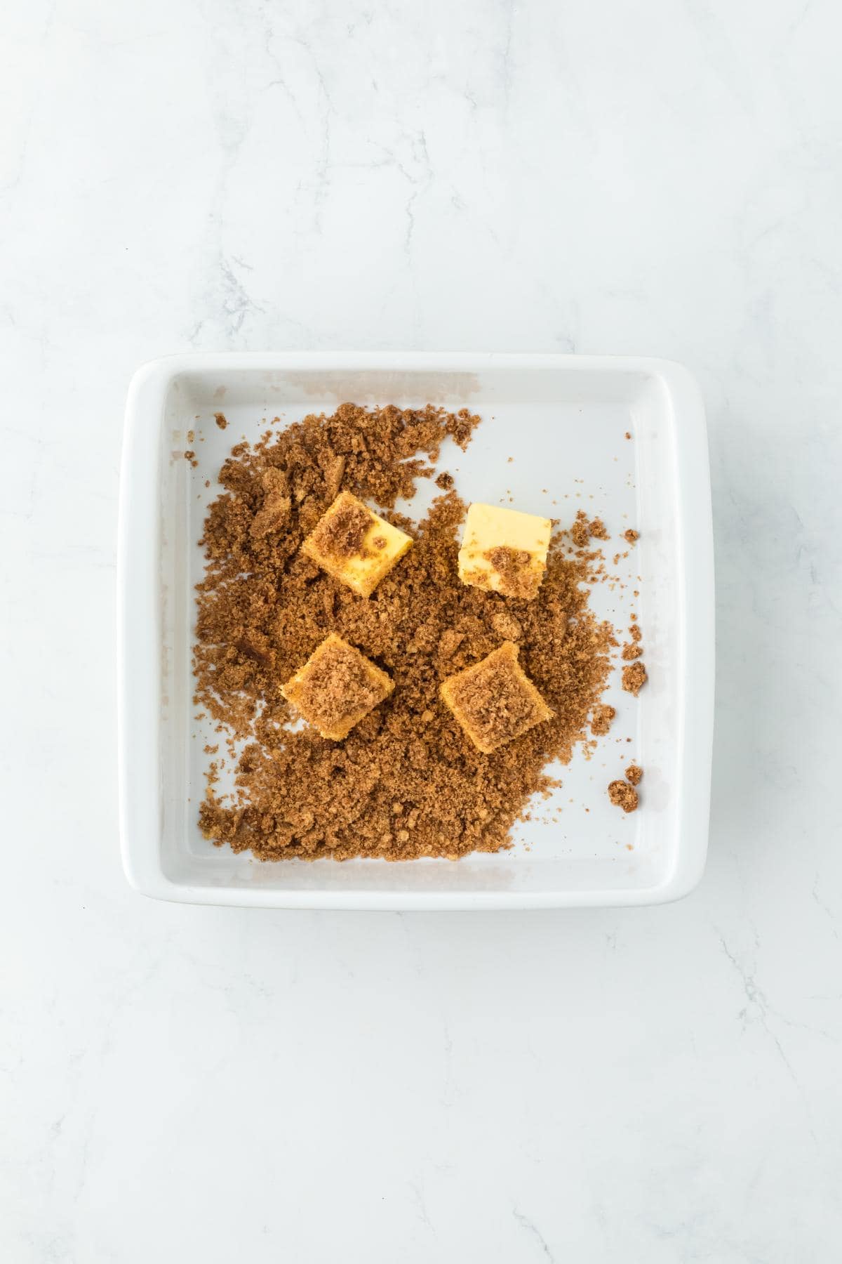 A baking dish with cubes of butter and a layer of brown sugar mixture scattered around