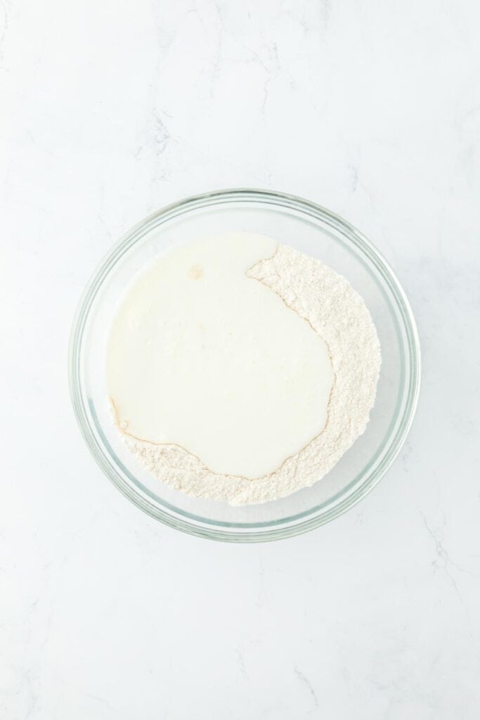 A glass bowl with buttermilk added to the dry ingredients, ready to be combined