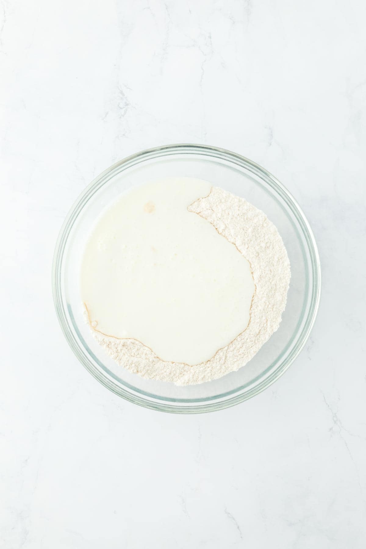 A glass bowl with buttermilk added to the dry ingredients, ready to be combined