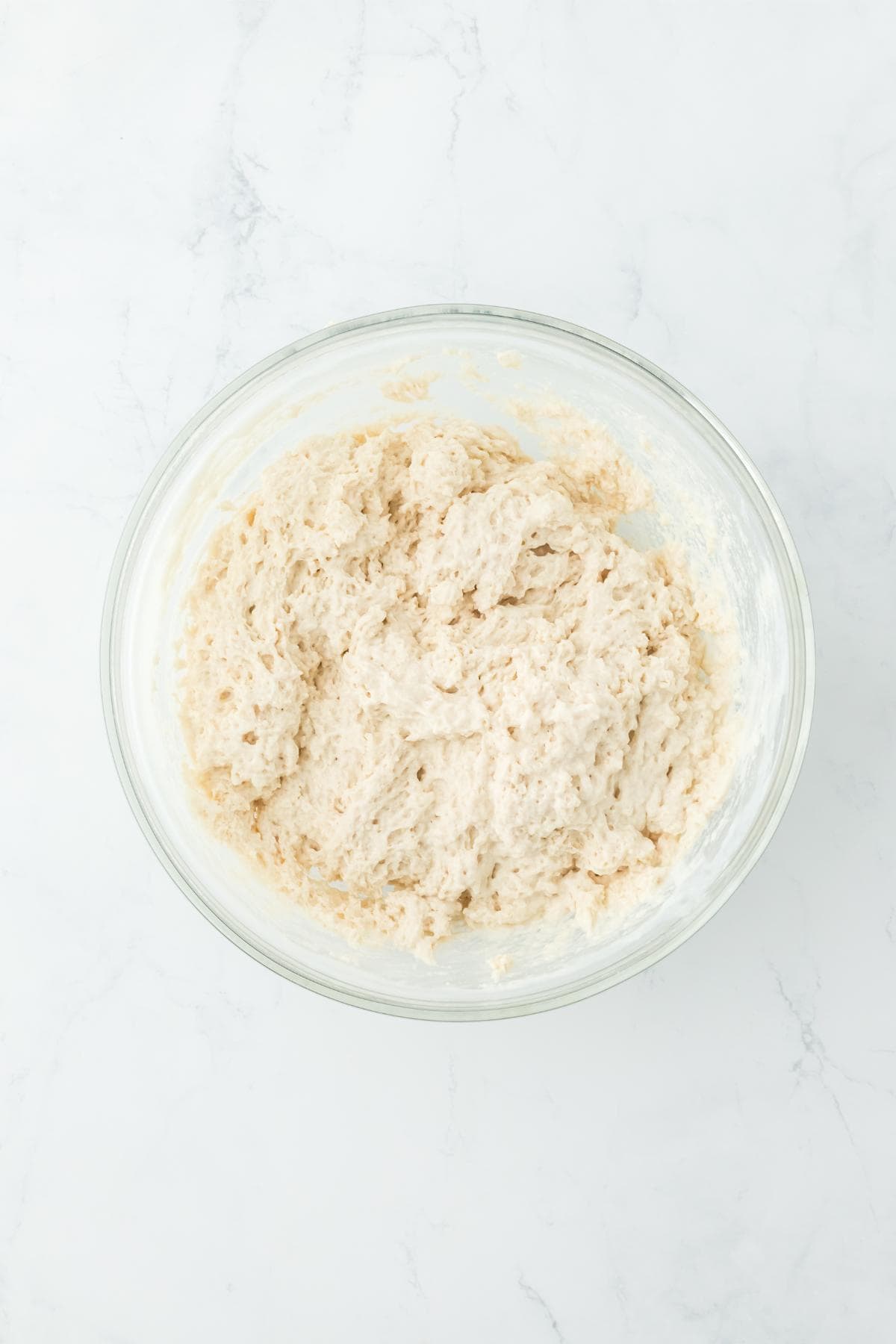 A glass bowl showing a mixed, sticky biscuit dough after combining the wet and dry ingredients