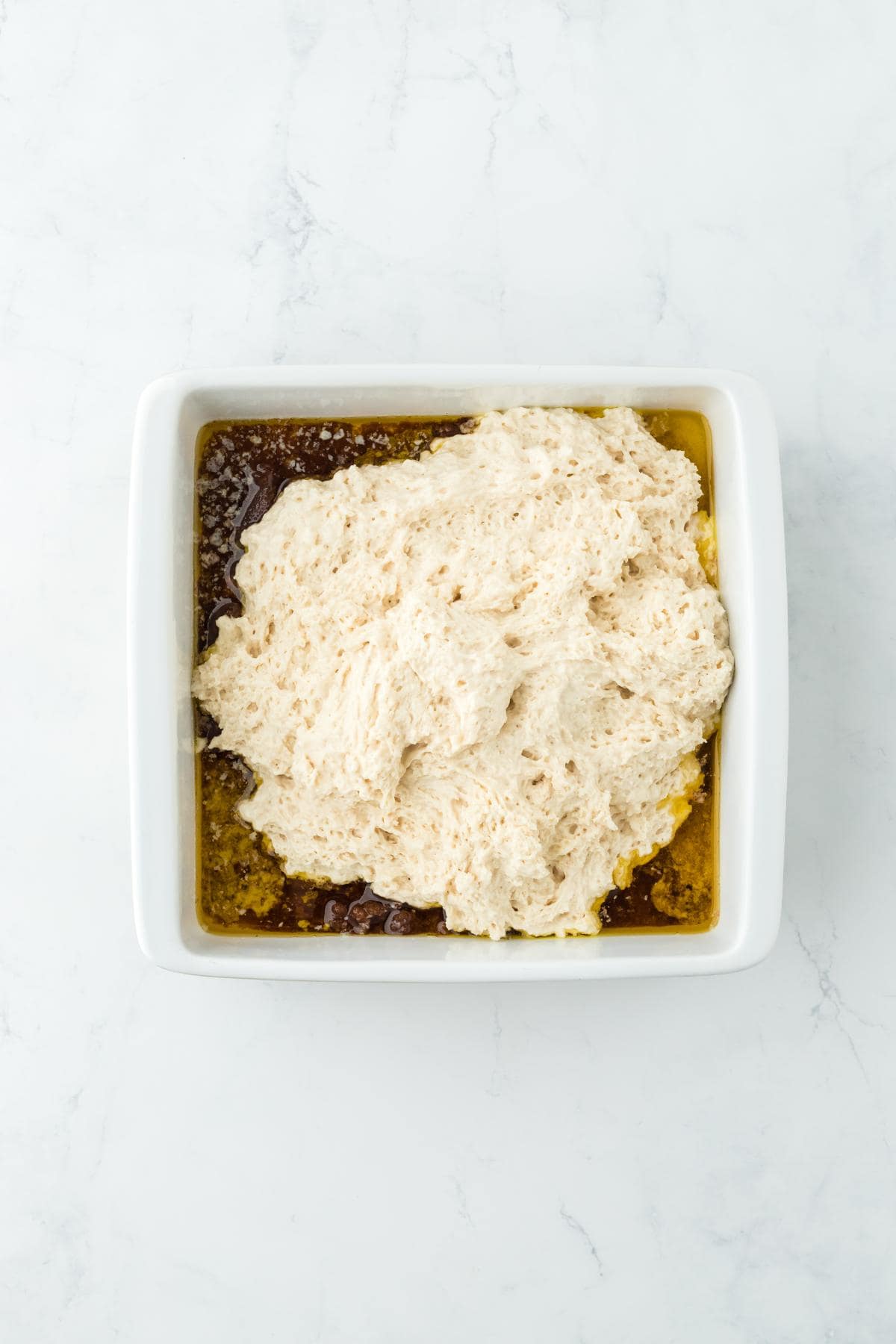 A baking dish with the prepared biscuit dough spread over the brown sugar and butter base