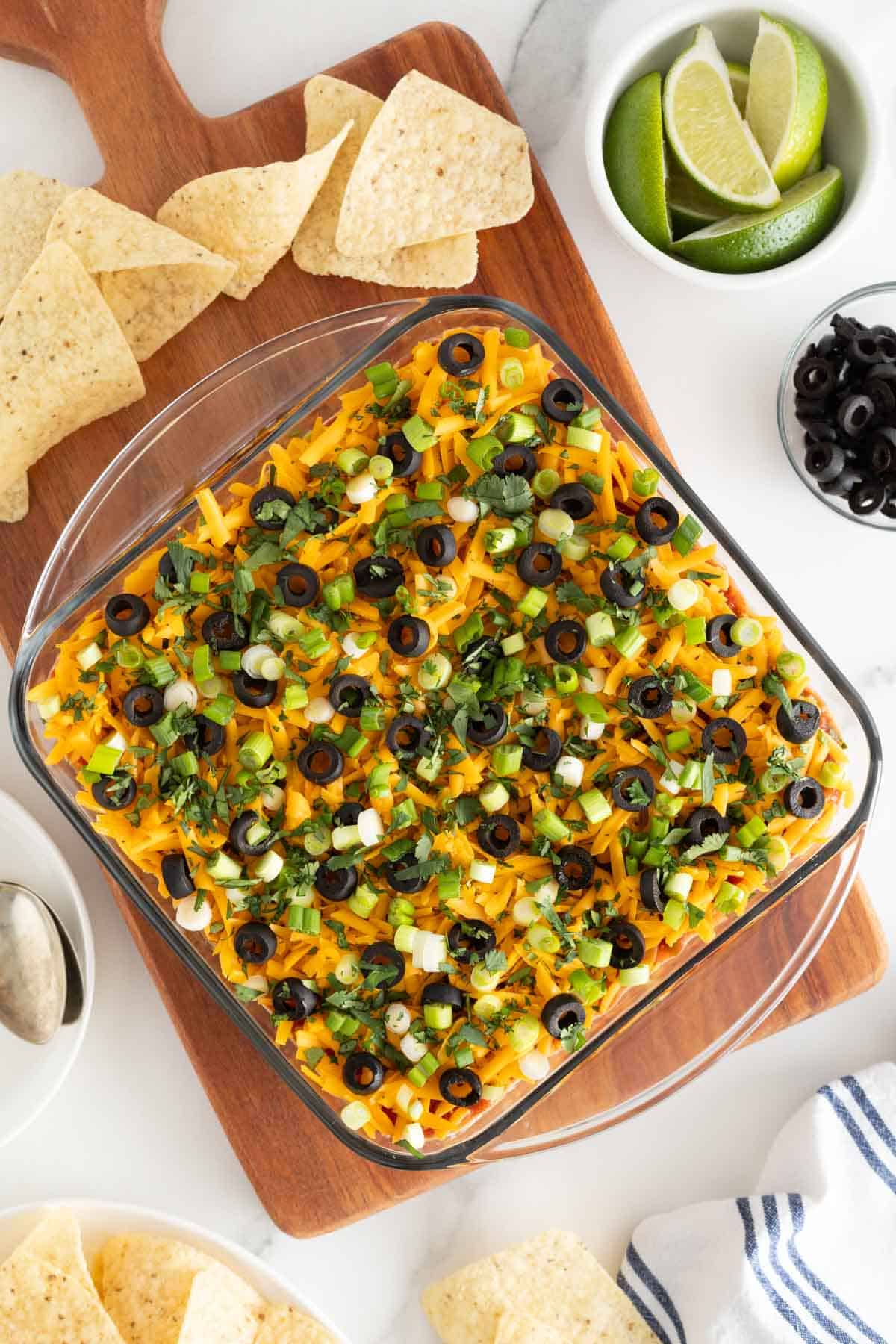 An overhead shot of 7 layer dip recipe with tortilla chips nearby with chips