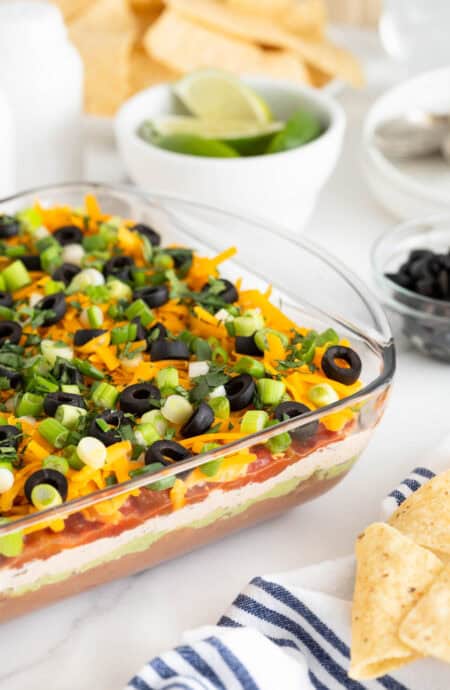 7 layer dip in a glass dish on a white countertop with chips