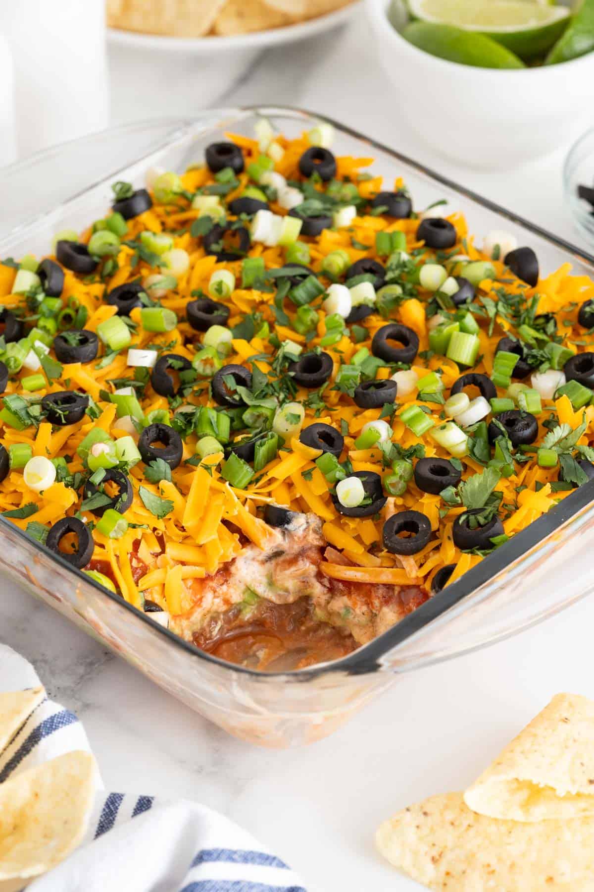 7 layer bean dip recipe with some eaten from a dish on white countertop