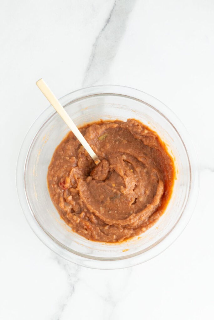 Salsa and refried beans being mixed together in a glass bowl