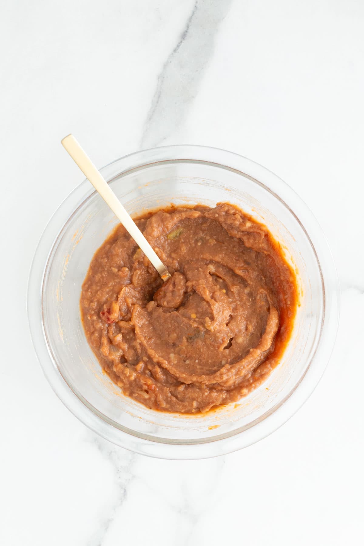 Salsa and refried beans being mixed together in a glass bowl