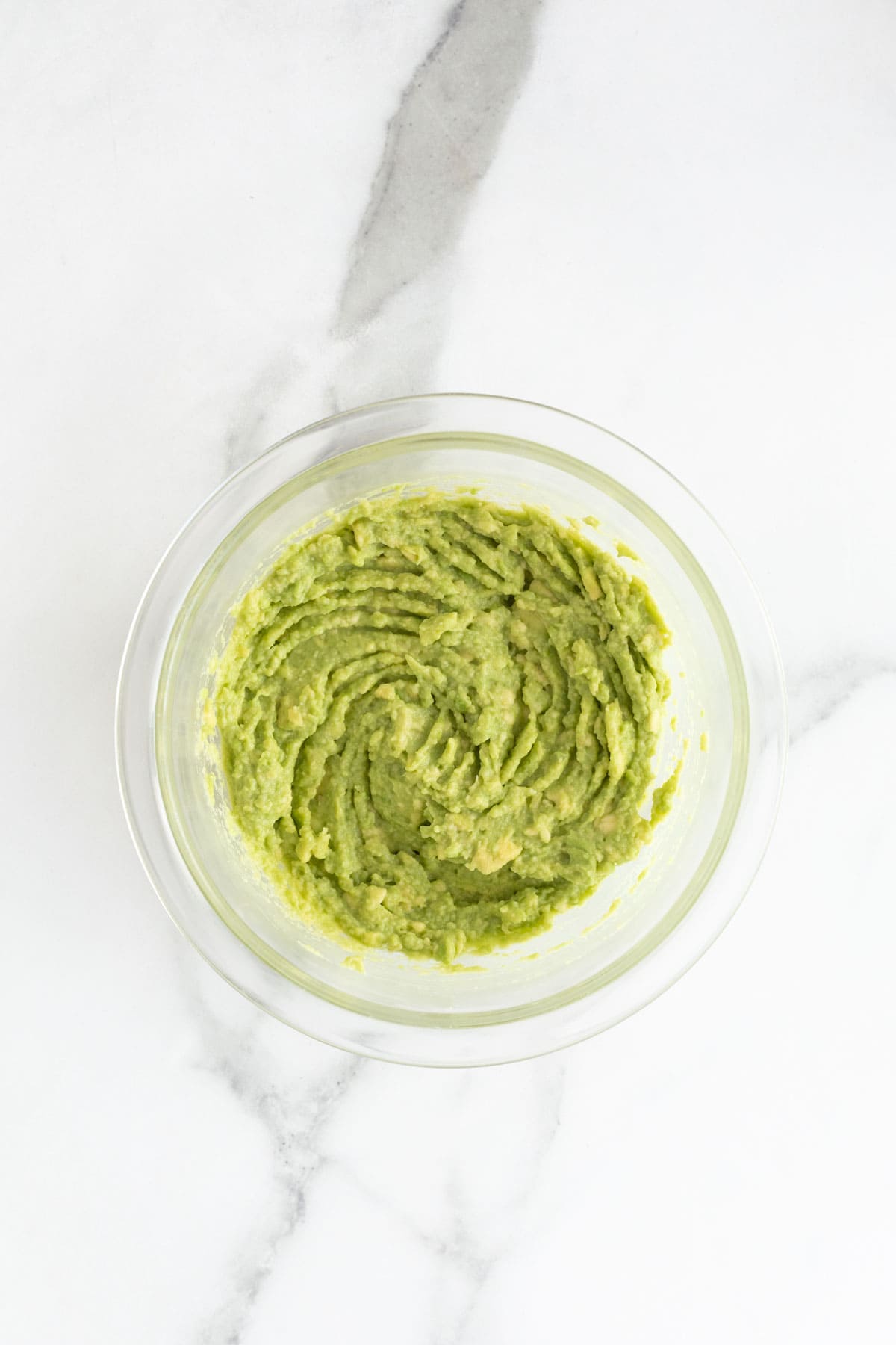 Mashed avocados with lime juice in a glass bowl on white countertop