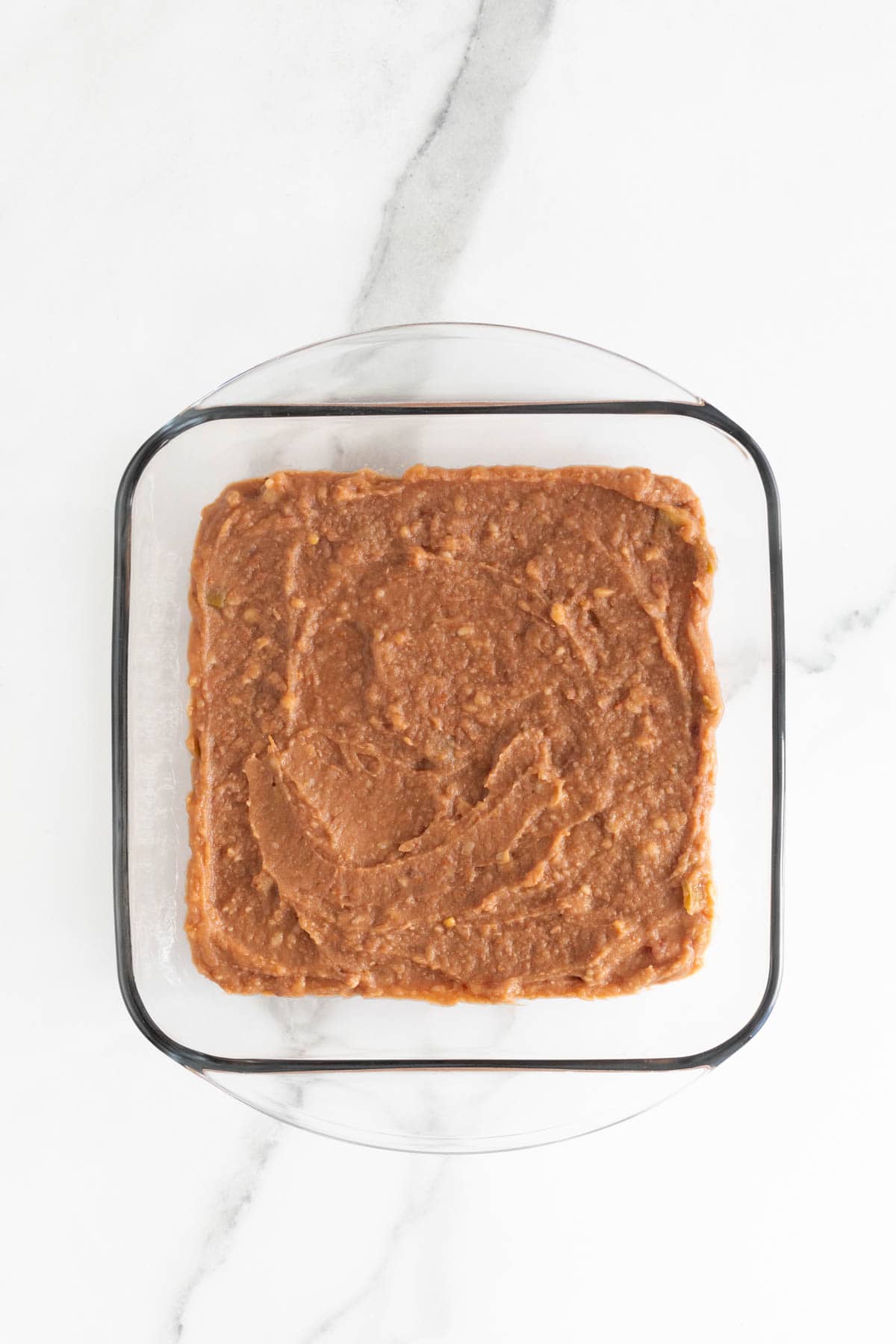 Refried beans spread on the bottom of a glass dish