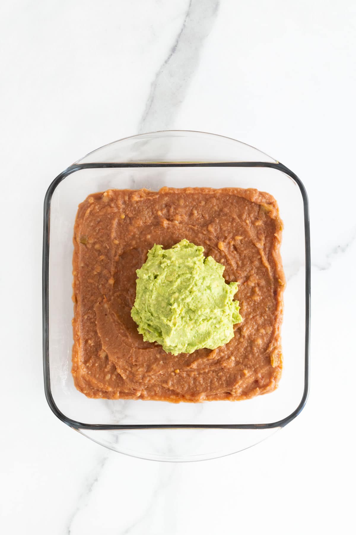 Guacamole added to top of spread out refried beans in dish