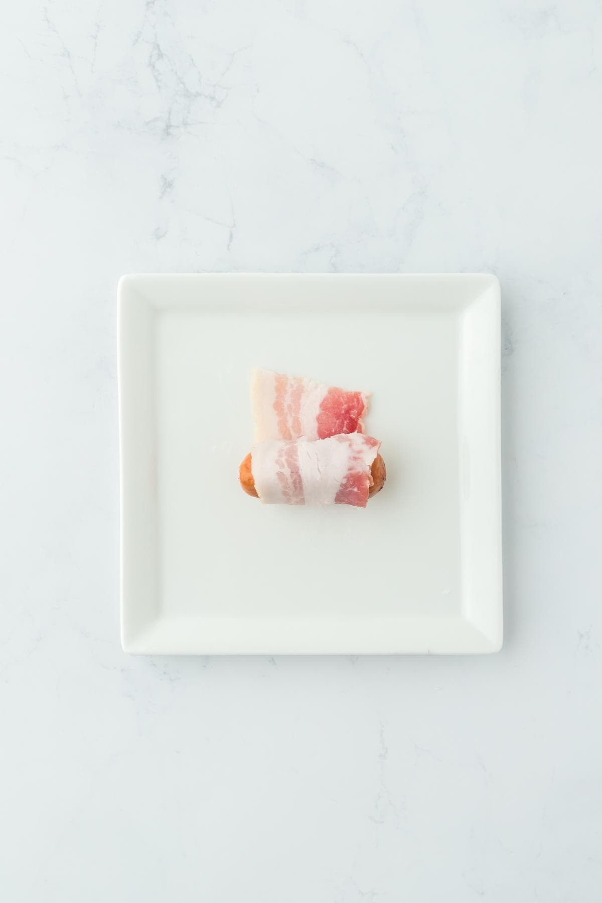 A plate with a cocktail sausage wrapped in bacon