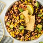 Closeup of cowboy caviar in a white bowl with a lime wedge and tortilla chips dipped into it