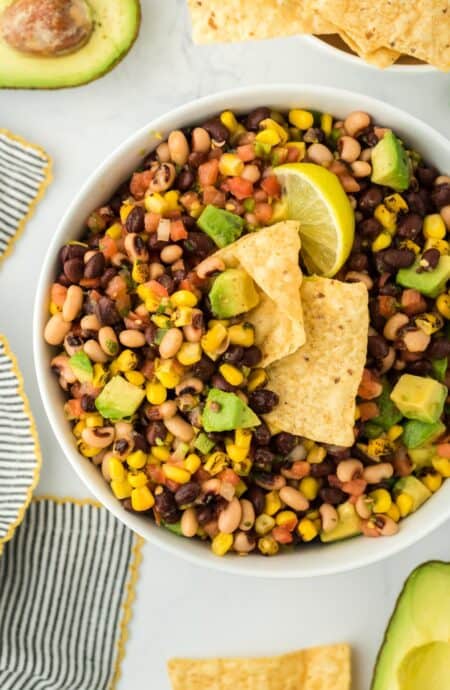 Closeup of cowboy caviar in a white bowl with a lime wedge and tortilla chips dipped into it