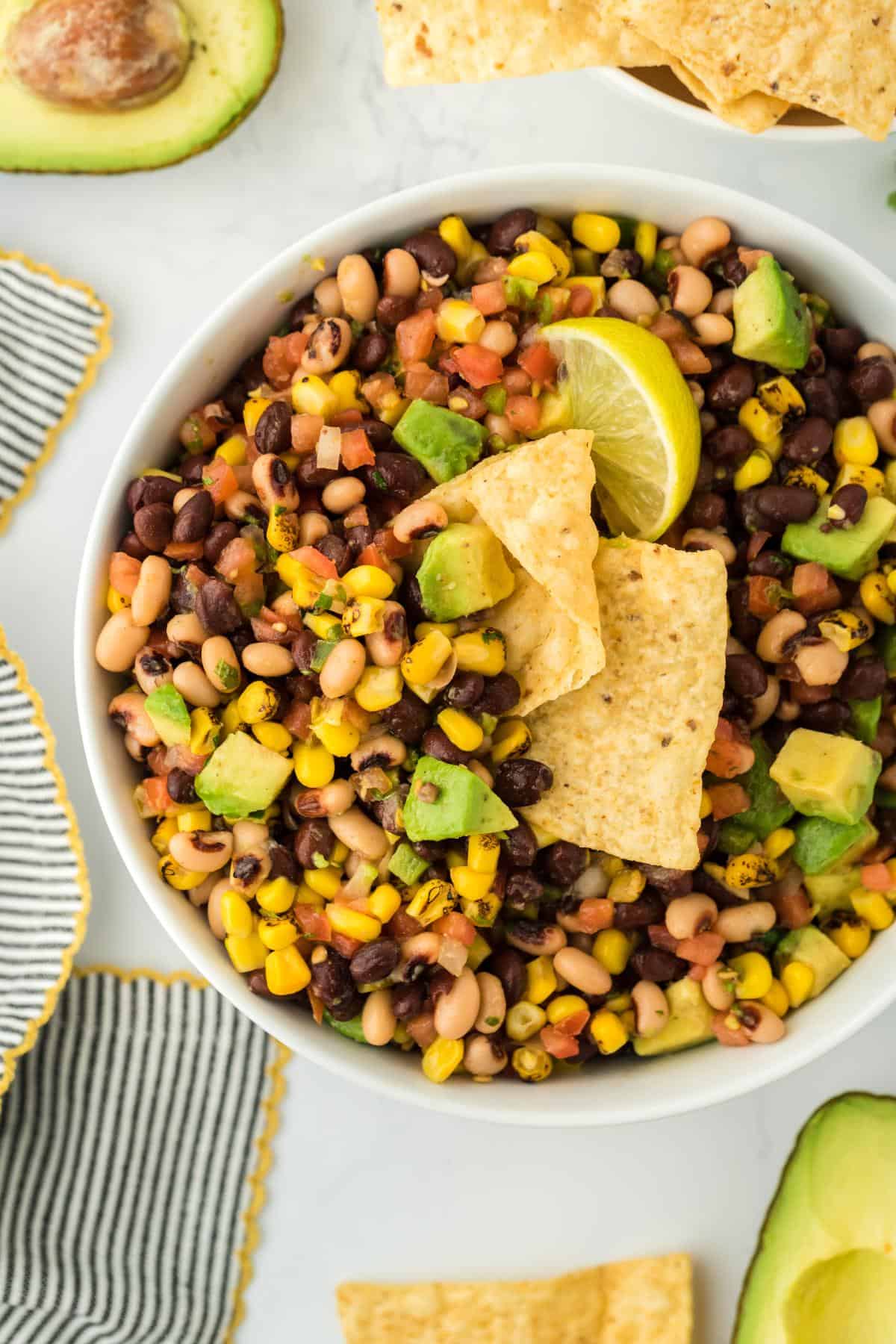 Closeup of cowboy caviar in a white bowl with a lime wedge and tortilla chips dipped into it