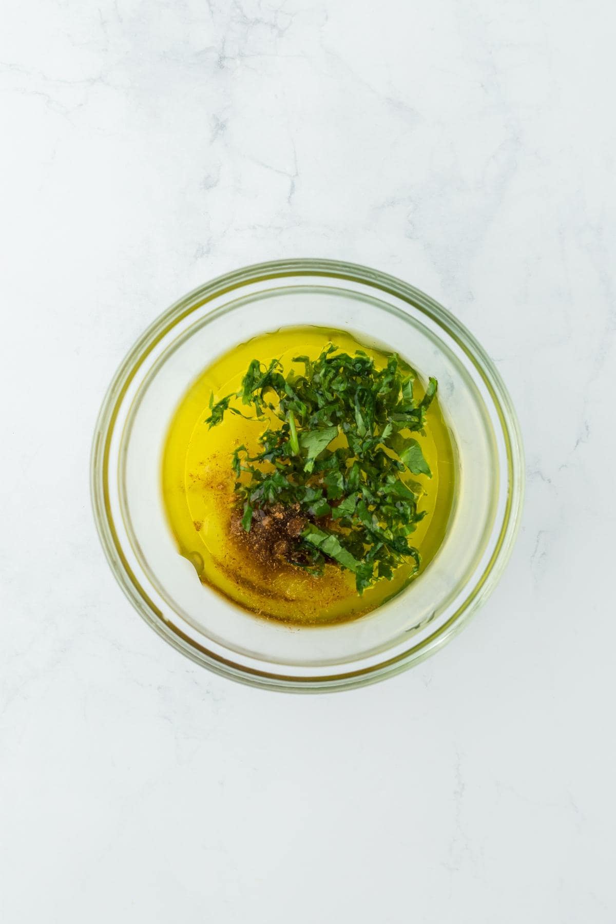 A glass bowl filled with olive oil, chopped cilantro, and seasonings