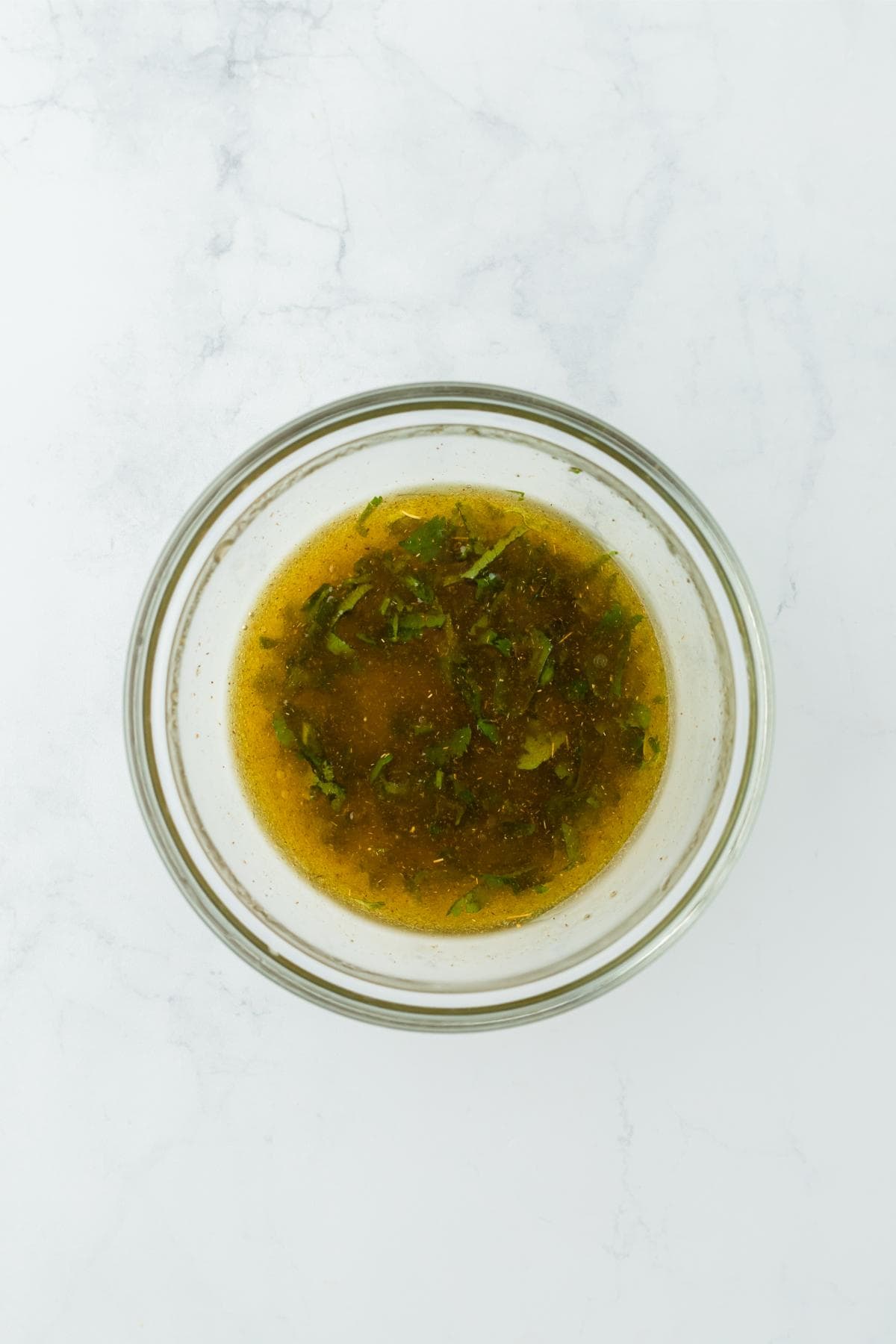 A glass bowl with the olive oil and cilantro mixture fully combined