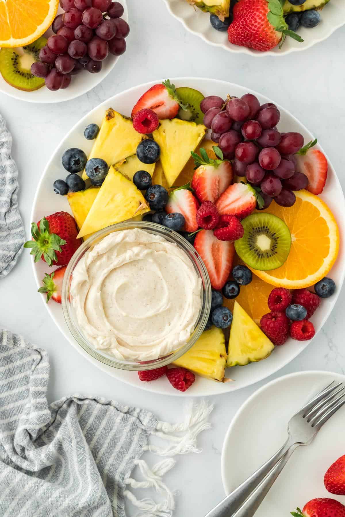 Overhead shot of a fruit platter featuring pineapple, strawberries, blueberries, raspberries, kiwi, and orange slices, arranged around a bowl of cream cheese fruit dip