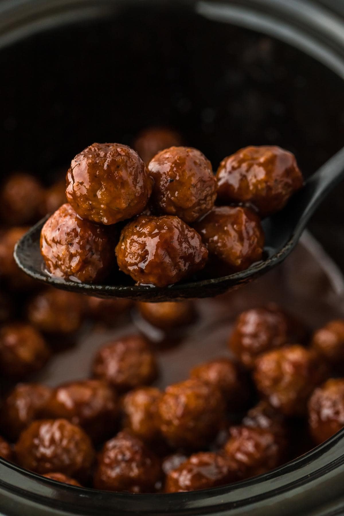 A spoonful of grape jelly meatballs lifted from the slow cooker, showcasing their shiny glaze