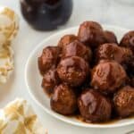 Plate of grape jelly meatballs served with a jar of grape jelly in the background and a fork next to it