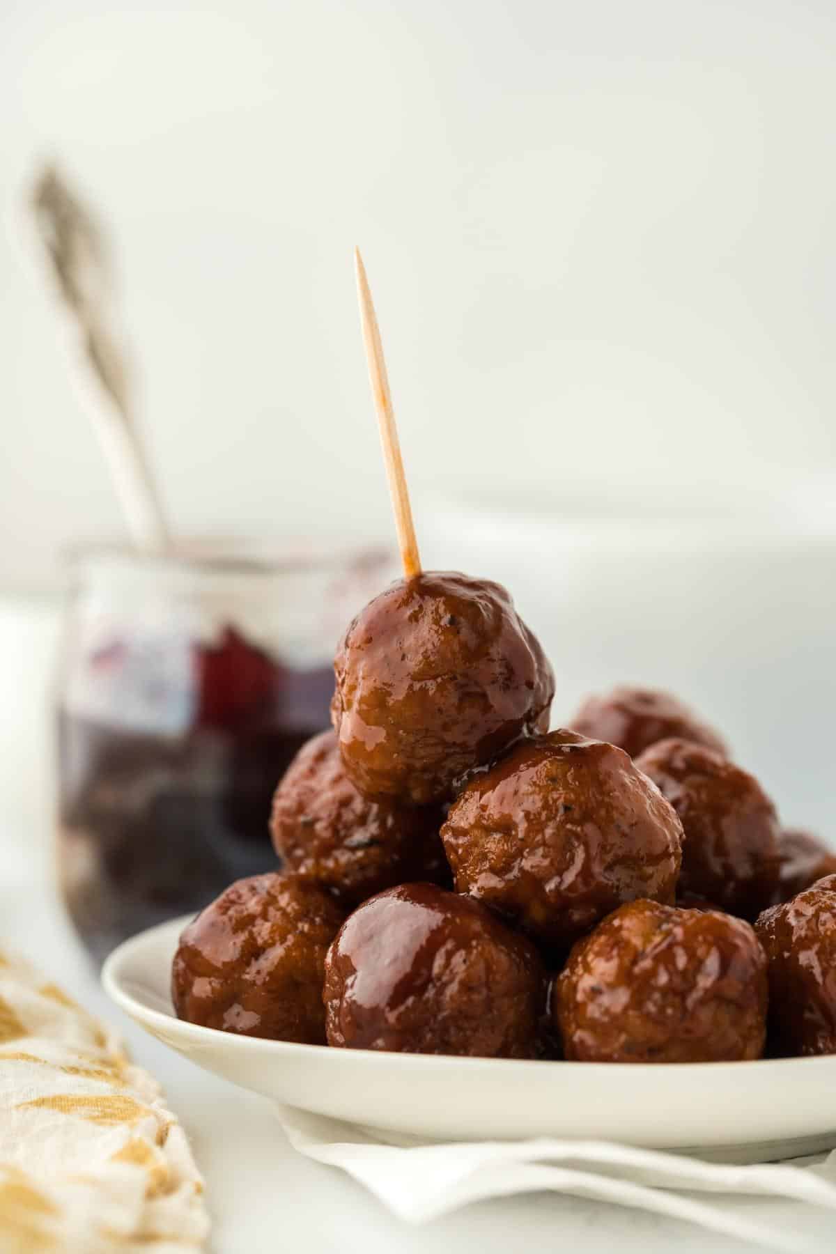 Side view of a stack of grape jelly meatballs on a plate, garnished with a toothpick on the top one