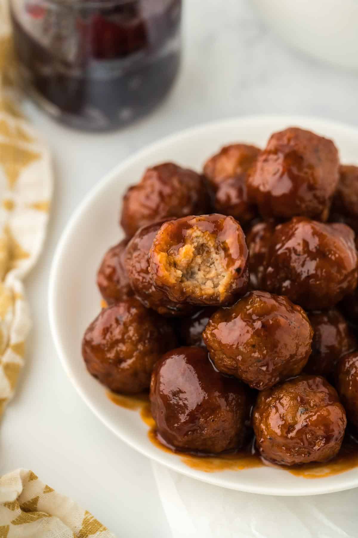 Plate of grape jelly meatballs with one bitten into, revealing the tender interior and saucy exterior