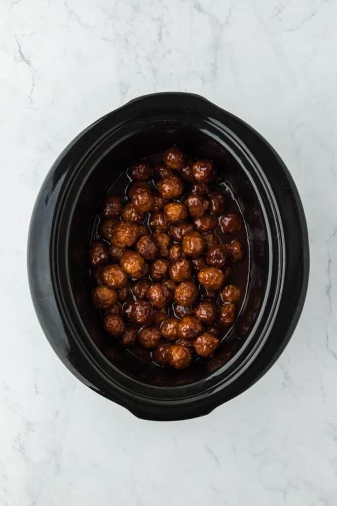 Closeup of fully cooked meatballs coated in a glossy grape jelly glaze inside the slow cooker
