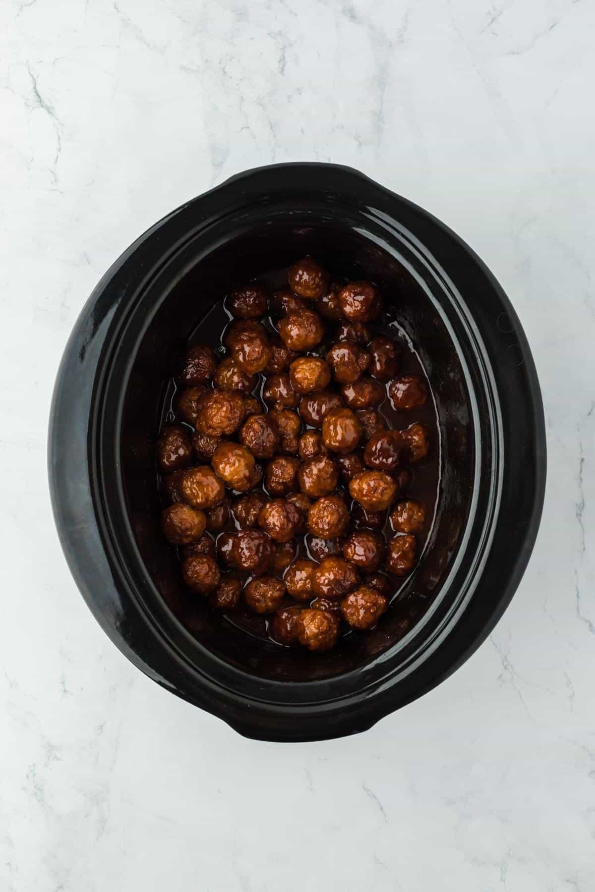 Closeup of fully cooked meatballs coated in a glossy grape jelly glaze inside the slow cooker