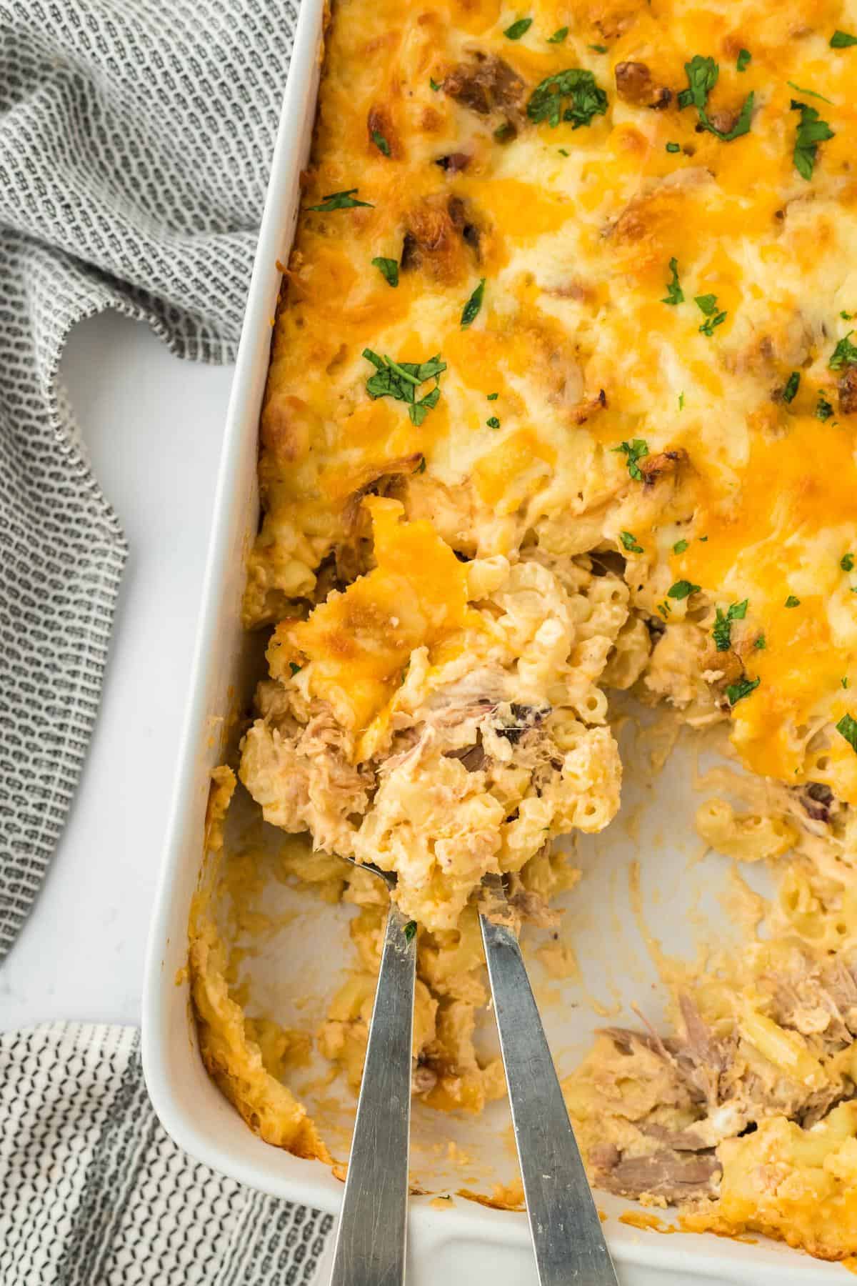 Overhead shot of two spoons scooping a serving of the pulled pork mac and cheese off the casserole dish