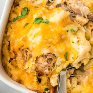 A spoon scooping a serving of the pulled pork mac and cheese off a casserole dish, showing the creamy macaroni and pulled pork filling